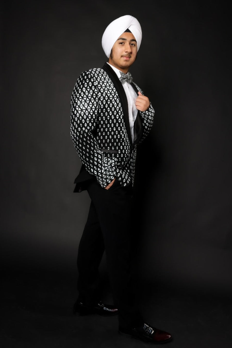 Man wearing a patterned black and white blazer with a white turban against a dark background